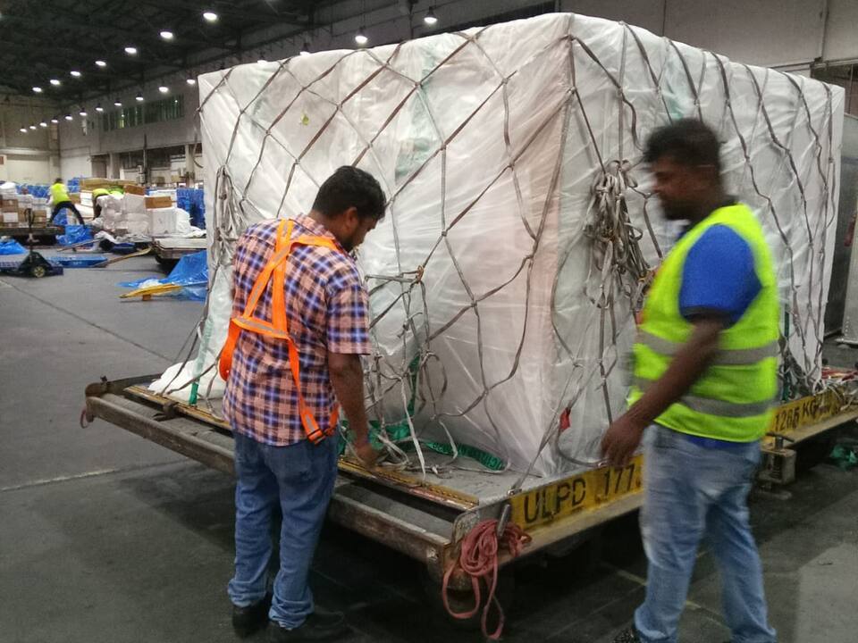 Two workers checking the net on a wrapped cargo pallet on a dolly