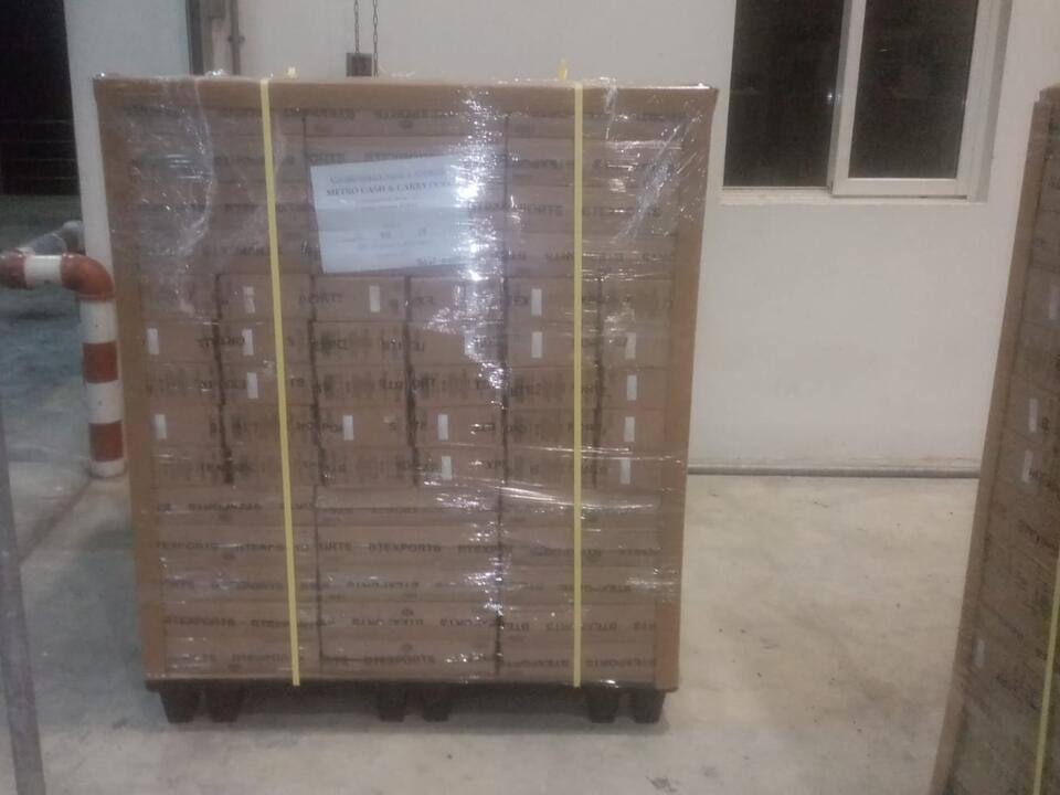 A tall pallet of cartons, shrink-wrapped and secured with yellow straps