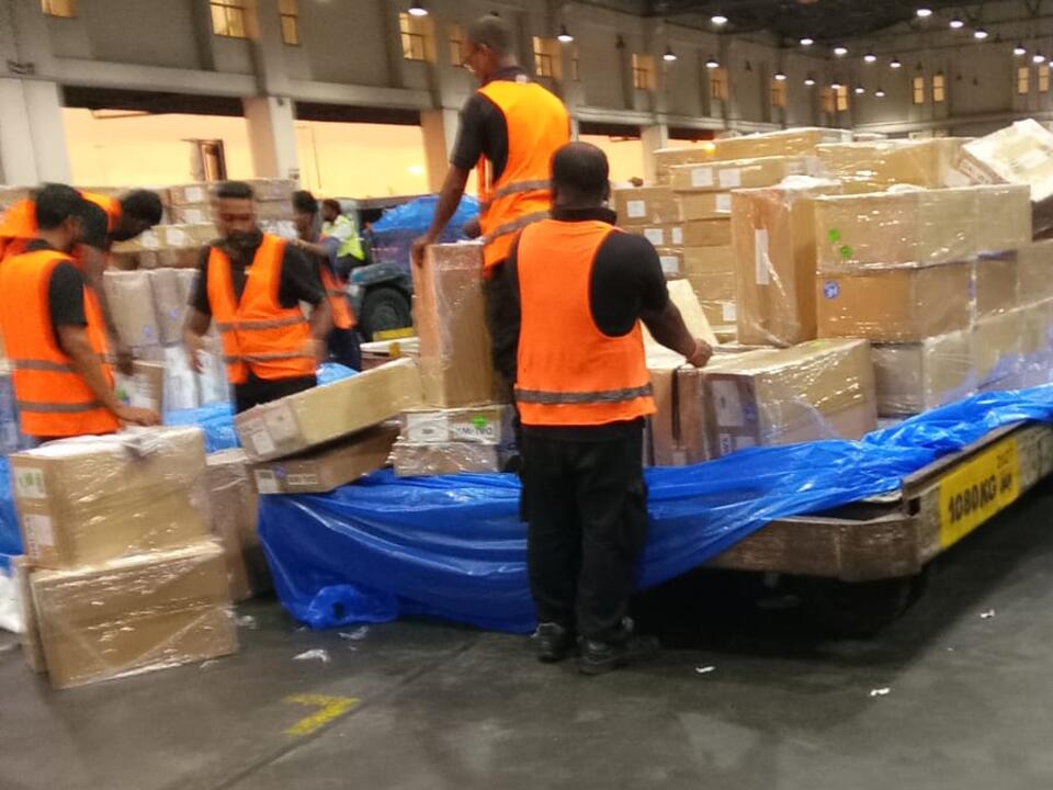 Workers in high-visibility vests stacking cartons onto a cargo pallet